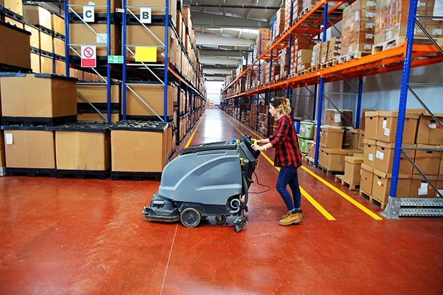 Employee using cleaning equipment in a warehouse