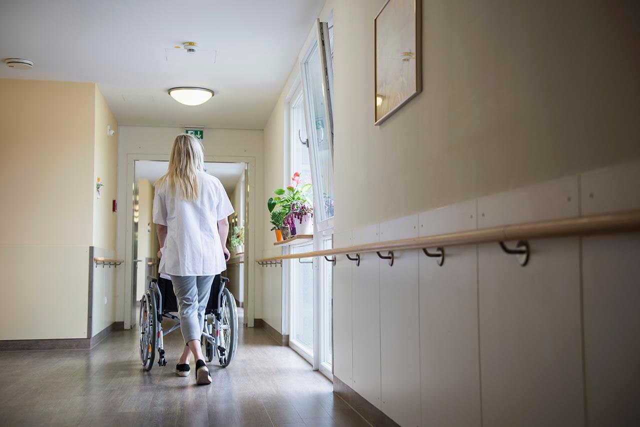 Care worker pushing a wheelchair down a corridor